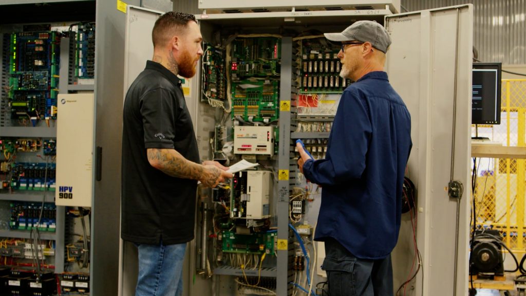 Two technicians standing by an elevator controller